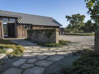 the outside of a rustic house with a walkway through it, a large stone courtyard and two wooden entry doors leading to an open kitchen