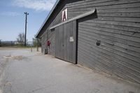 a large gray building with a black front door and a red window on top of a wooden garage