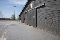 a large gray building with a black front door and a red window on top of a wooden garage