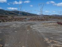 an empty field with power lines and dirt on the ground with blue skies in the background