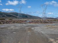 an empty field with power lines and dirt on the ground with blue skies in the background