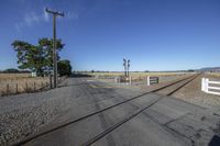 an empty street with railroad tracks and train crossing on it in the rural area of an area with a dirt lot