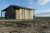 a small shed with roof missing sits in a field covered in dirt and grass and mud