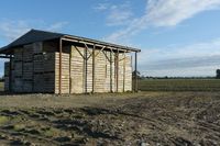 a small shed with roof missing sits in a field covered in dirt and grass and mud