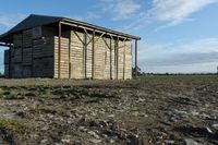 a small shed with roof missing sits in a field covered in dirt and grass and mud