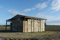 a small shed with roof missing sits in a field covered in dirt and grass and mud