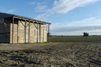 a wooden building sitting next to a big field with green grass growing outside of it