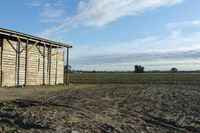 a wooden building sitting next to a big field with green grass growing outside of it