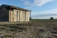 a wooden building sitting next to a big field with green grass growing outside of it