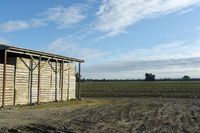 a wooden building sitting next to a big field with green grass growing outside of it