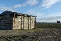 a wooden building sitting next to a big field with green grass growing outside of it