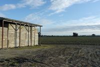 a wooden building sitting next to a big field with green grass growing outside of it