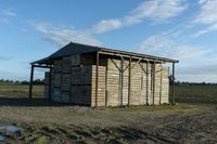 a wooden building sitting next to a big field with green grass growing outside of it