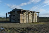 a wooden building sitting next to a big field with green grass growing outside of it