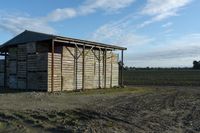 a wooden building sitting next to a big field with green grass growing outside of it