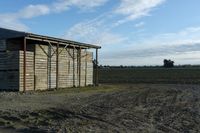 a wooden building sitting next to a big field with green grass growing outside of it