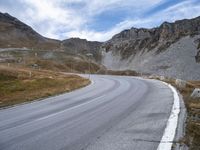 a winding road runs between a few rocky hills in the background are hills and mountains