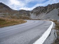 a winding road runs between a few rocky hills in the background are hills and mountains