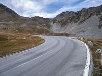 a winding road runs between a few rocky hills in the background are hills and mountains