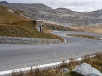 an old stone building sitting in the middle of a winding road next to a mountain