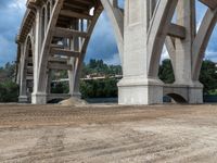 a bridge being built with dirt and a blue sky above it and green trees below