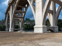 a bridge being built with dirt and a blue sky above it and green trees below