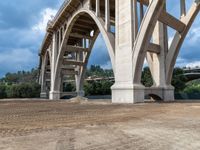 a bridge being built with dirt and a blue sky above it and green trees below