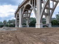 a dirt road with a large bridge in the background under construction at a construction site