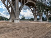 a dirt field under a bridge next to trees and a street light sign saying, no parking