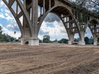 a dirt field under a bridge next to trees and a street light sign saying, no parking