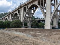 a construction site with a road and bridge in the background a hill with some trees, grass, dirt, and dirt