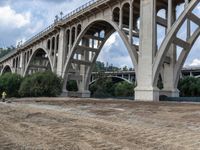 a construction site with a road and bridge in the background a hill with some trees, grass, dirt, and dirt