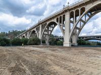 a construction site with a road and bridge in the background a hill with some trees, grass, dirt, and dirt