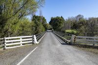 a white wooden bridge with a fence and trees on both sides and a road through