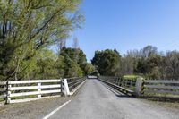 a white wooden bridge with a fence and trees on both sides and a road through