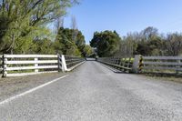 a white wooden bridge with a fence and trees on both sides and a road through