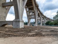 an overpass of bridge construction in the middle of the day with a person standing on a dirt field underneath it