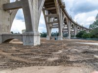 an overpass of bridge construction in the middle of the day with a person standing on a dirt field underneath it