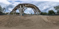 a very wide and high looking bridge that is over some dirt hill side, as clouds in the sky