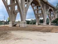 a man sitting in a dirty field under an overpass bridge next to a road with a truck on it