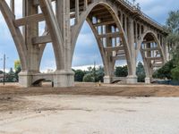 a man sitting in a dirty field under an overpass bridge next to a road with a truck on it