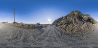 a dirt road passing by the dirt wall, in front of the sun in a rural setting