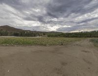 the view from the corner of a dirt road with dirt road and hills in the background