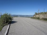 a lone highway on the hillside with a small shrub and mountains in the distance of it