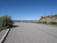 a lone highway on the hillside with a small shrub and mountains in the distance of it