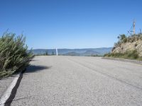 a lone highway on the hillside with a small shrub and mountains in the distance of it