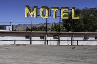 a motel sign in a deserted lot with mountains in the background, taken from a car window