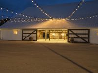 a barn with twinkle lights hanging from the roof and door, and outside it is a covered patio area