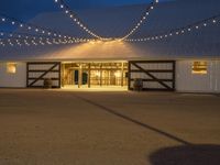 a barn with twinkle lights hanging from the roof and door, and outside it is a covered patio area