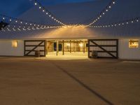 a barn with twinkle lights hanging from the roof and door, and outside it is a covered patio area